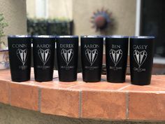 six black tumblers are lined up on a brick ledge