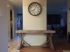 a clock mounted on the wall above a wooden table in a room with tile flooring