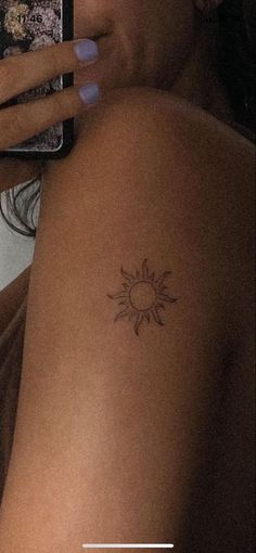 a woman with a sun tattoo on her arm holding a cell phone and taking a selfie