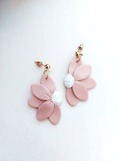 two pink and white flower shaped earrings on top of a table next to each other