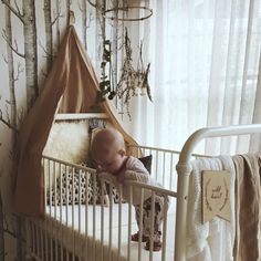 a baby sleeping in a white crib next to a wall with trees on it