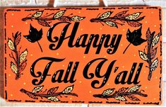 an orange happy fall sign hanging on a brick wall with leaves and acorns