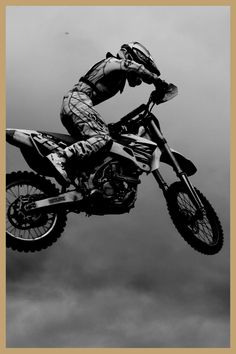 black and white photograph of a person on a dirt bike in the air with clouds behind them