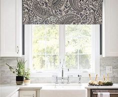 a kitchen with a sink and window covered in blue paisley print roman shades over the windows