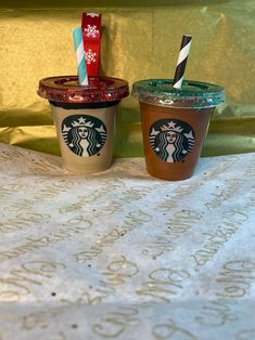 two starbucks cups sitting on top of a table next to each other with straws in them