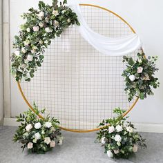 two white flowers and greenery arranged in front of a circular backdrop