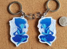 two keychains with cartoon characters on them sitting next to one another and a coin