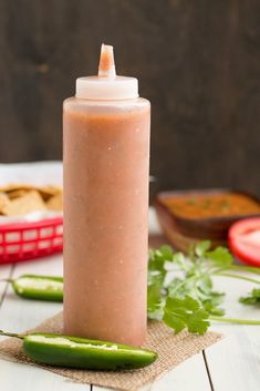 a bottle filled with sauce sitting on top of a table next to sliced green peppers