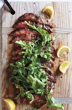 a steak with greens and lemon slices on a cutting board