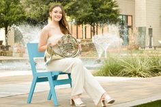 a woman sitting on a blue chair holding a french horn in front of a fountain