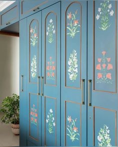 a blue cabinet with flowers painted on the side and gold trimmings, along with a potted plant