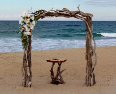 an arch made out of driftwood and flowers on the beach with waves in the background