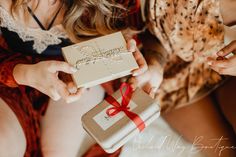 two women are holding small gifts wrapped in brown paper and red ribbon, with one woman's hand on top of the box