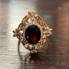 a fancy ring with a large red stone surrounded by small white and yellow diamonds on a wooden surface