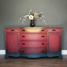 a vase with flowers sitting on top of a red and blue dresser against a gray wall