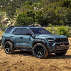 a blue truck parked on top of a dirt field next to some rocks and trees