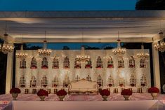 an outdoor wedding setup with chandeliers and red flowers on the table at night