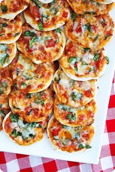 small pizzas with cheese and spinach on a white plate next to a red checkered tablecloth