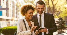 a man and woman are looking at their cell phones while walking down the street together