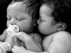 two babies laying next to each other with their faces close together and one holding a pacifier