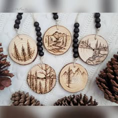 four wood burned ornaments with pine cones and beads on a white tablecloth, surrounded by pine cones