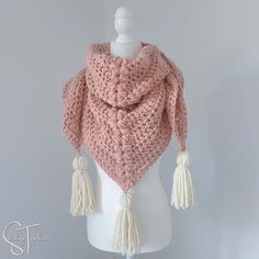 a white mannequin wearing a pink crochet shawl with tassels