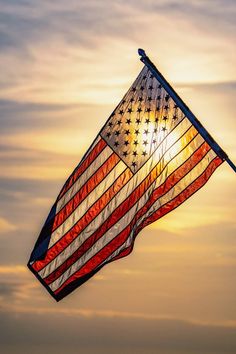 an american flag flying in the sky at sunset