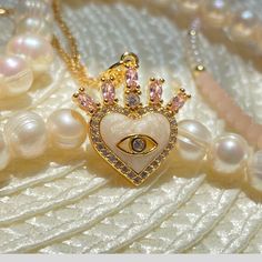 "Heart Evil Eye Necklace with Crown and Pink Stones.  Introducing our stunning 18k gold filled Crown Evil Eye Heart Necklace, a one-of-a-kind piece of jewelry that is sure to turn heads. Crafted from high-quality materials, this necklace features a beautifully intricate crown design, adorned with sparkling cubic zirconia stones, that sits atop a striking heart-shaped evil eye pendant. The pendant is carefully handcrafted with a beautiful emerald pink stone, a powerful symbol of protection and good fortune. Made with 18k gold filled chain that is both durable and resistant to tarnishing, this necklace is perfect for everyday wear and will last you for years to come. Whether you're looking to add a touch of elegance to your work outfit or to make a statement on a night out, this necklace is Handmade Rose Gold Heart Pendant Jewelry, Dainty Heart-shaped Cubic Zirconia Charm Necklace, Gold Plated Heart Shaped Jewelry For Her, Heart-shaped Gold Plated Jewelry For Her, Heart-shaped Gold Plated Jewelry As Gift For Her, Heart Shaped Gold Plated Jewelry As Gift For Her, Dainty Handmade Jewelry For Valentine's Day, Handmade Dainty Heart-shaped Jewelry, Handmade Dainty Heart Shaped Jewelry