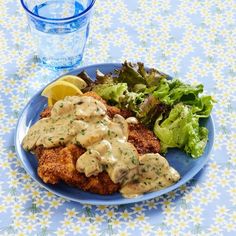 a blue plate topped with meat covered in gravy next to a salad and a glass of water