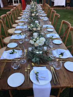 a long wooden table with white plates and flowers on it is set for a formal dinner