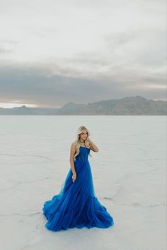 a woman in a blue dress is standing in the middle of an empty desert plain