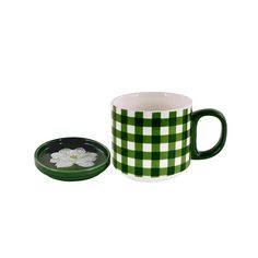 a green and white checkered coffee mug with a flower in the middle, sitting next to a plate