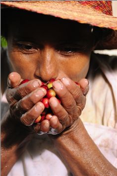 a woman wearing a straw hat and holding coffee beans in her hands, while looking at the camera