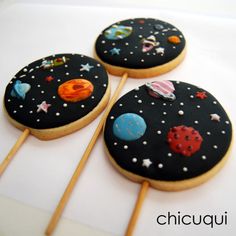 three decorated cookies sitting on top of each other next to toothpicks in the shape of planets