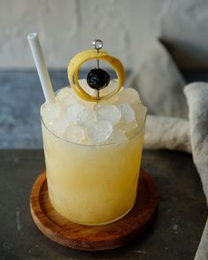 a drink with an orange slice on the rim and a straw in it sitting on a wooden coaster