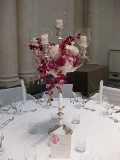 a centerpiece with flowers and candles on a white table cloth at a wedding reception