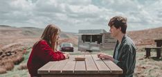 a man and woman sitting at a picnic table in front of a camper trailer