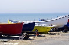 three boats are parked on the beach near the water and one is red, white and blue