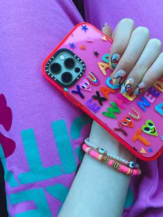 a woman holding a pink phone case with letters and numbers on the front, while wearing bracelets