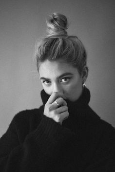 a black and white photo of a woman with her hand to her mouth looking at the camera