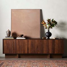 a vase with some flowers on top of a wooden cabinet next to a painting and other items