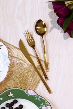 a plate with olives, fork and knife on it next to a purple flower