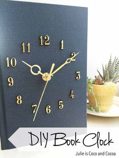 a clock made out of a book sitting on top of a table next to a potted plant