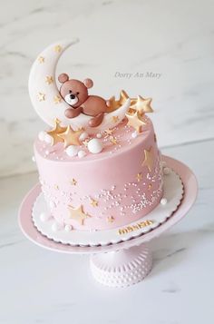 a pink cake with gold stars and a teddy bear sitting on top of the moon