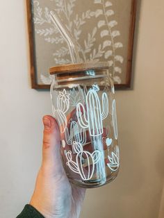 a person holding a glass jar with a straw in it that has cactus designs on it