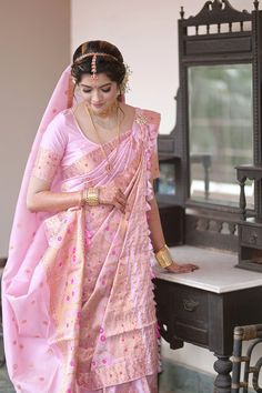 a woman in a pink and gold sari is looking down at her hand while standing next to a mirror