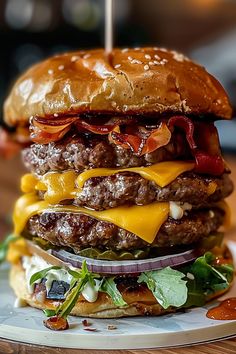 a cheeseburger with bacon, lettuce and onions on a bun sitting on a plate