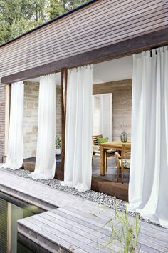 the outside of a house with white curtains on it's windows and wooden decking