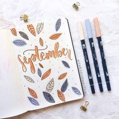 an open notebook with the word september written in orange and black on it next to two markers