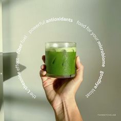 a hand holding a green drink in front of a white wall with words around it